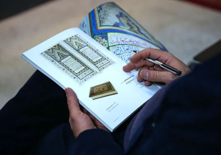 A specialist examining a work on paper under a desk lamp